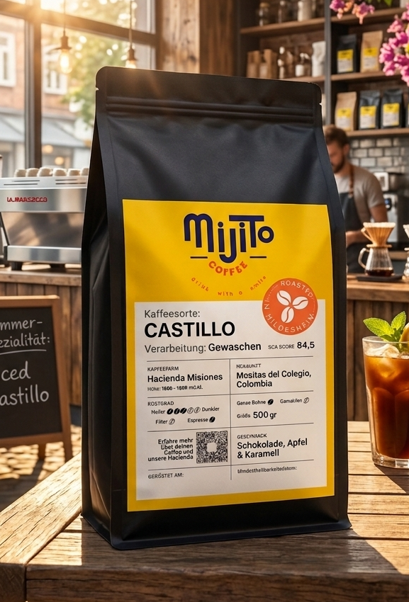 A black bag of Mijito Castillo coffee stands on a wooden table in a sunlit cafe setting, with a glass of iced coffee and hanging pink flowers in the background.