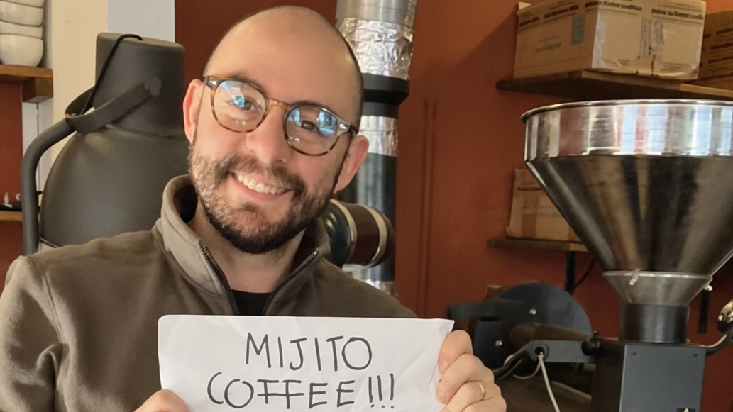 Person holding a sign with 'Mijito Coffee' in front of a coffee roasting machine.